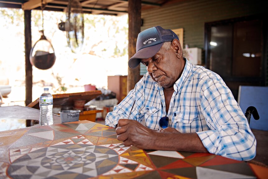An Indigenous man touches up one of his paintings