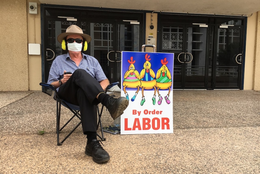 Gerry Wood sits in a chair with dark glasses and his mouth covered. He also has ear muffs on.