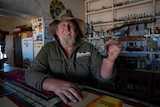 Robbo Haken is wearing a beat-up akubra and holding a Yabby from behind a bar