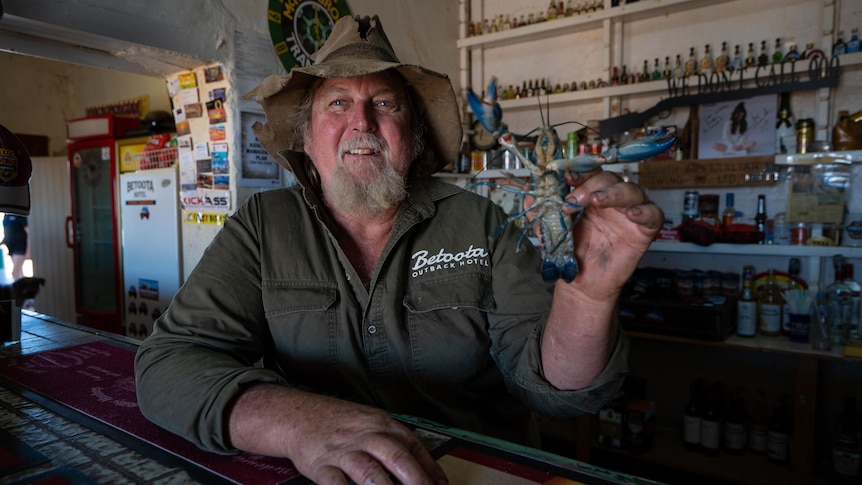 Robbo Haken is wearing a beat-up akubra and holding a Yabby from behind a bar