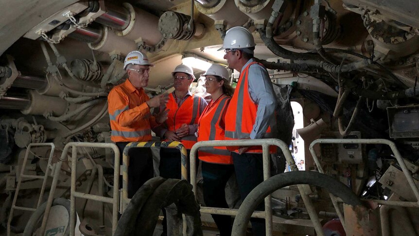 Four people in high viz and hard hats stand on the boring machine that is building a tunnel.