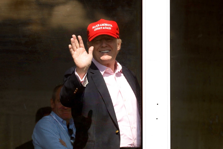 From behind a glass door, Donald Trump waves to patrons at his Trump National Golf Club in Bedminster, New Jersey.