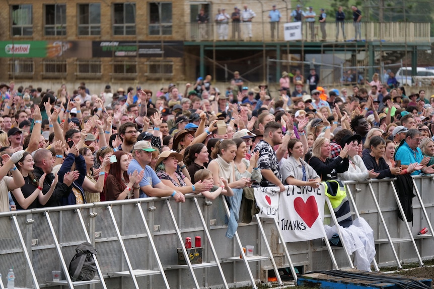 People standing crowded together at a barricade with their arms in the air, cheering.