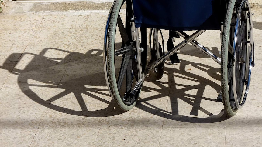 A wheelchair casts a shadow on a tiled floor.