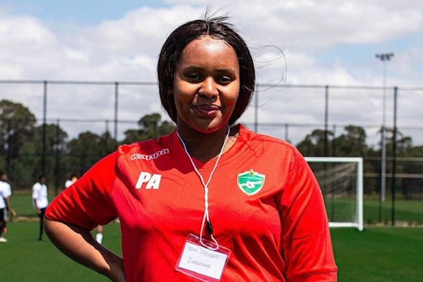 A woman wearing a red t-shirt has her hand on her hip, and smiles at the camera.