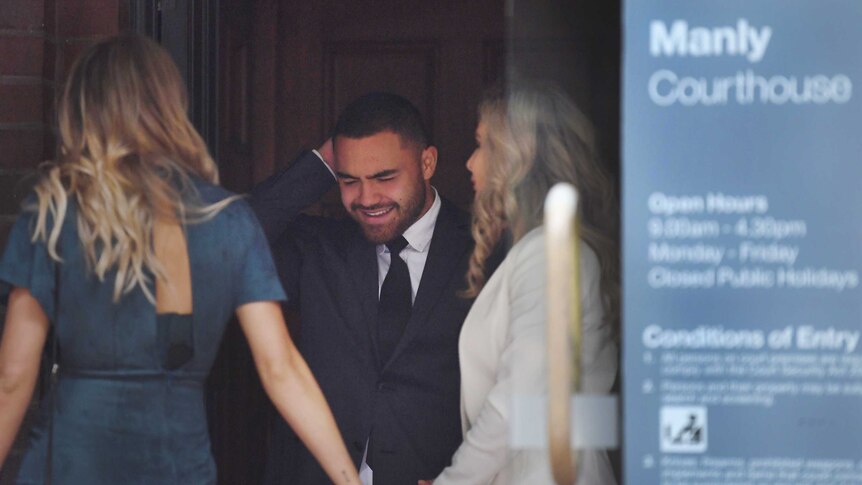 A smiling man stands in the entry of a courthouse, next to his partner and her mother.