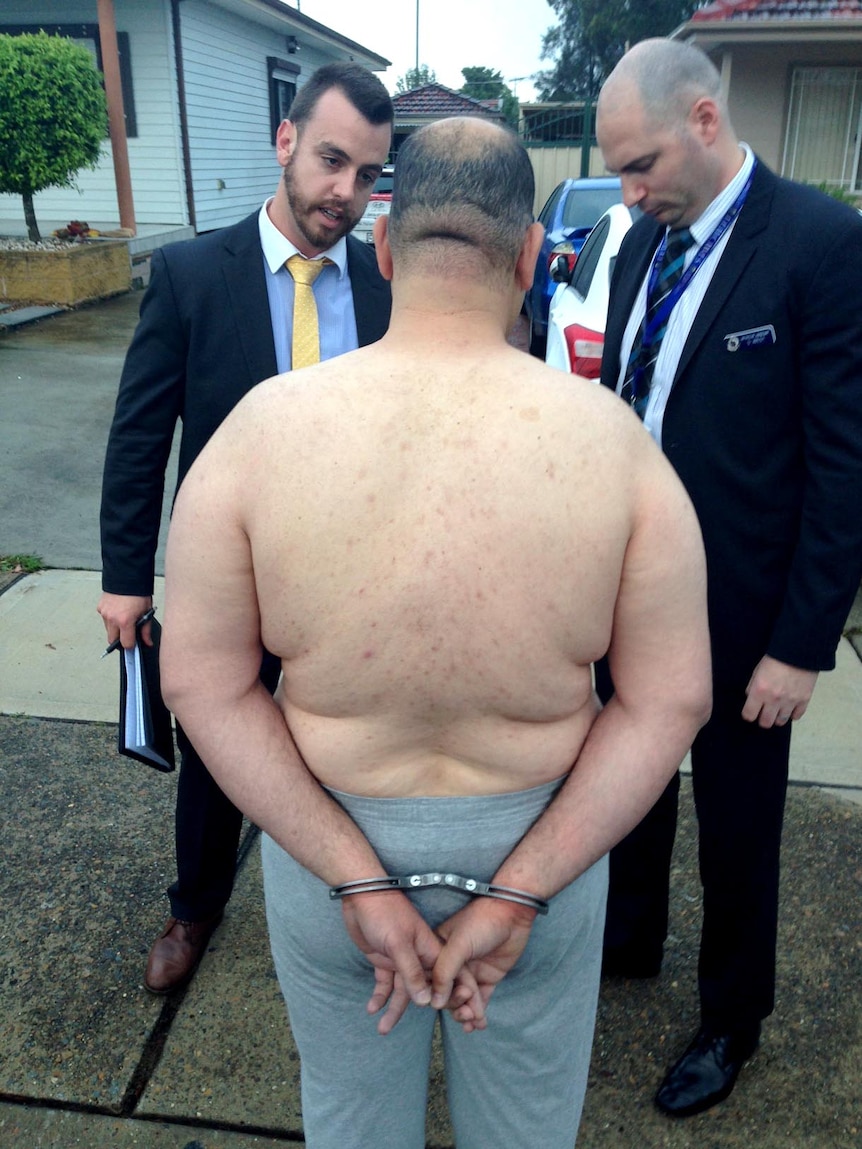 Police speak to a topless man during a dawn raids in Sydney's south west.