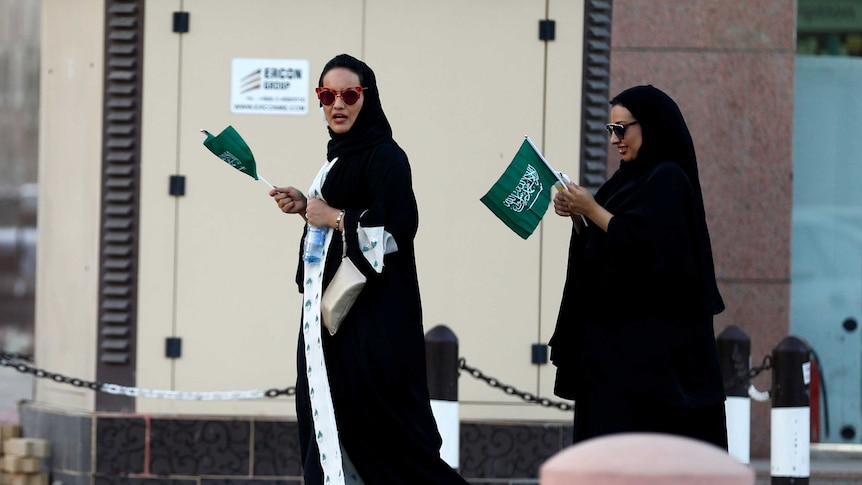 Saudi women hold national flags as they walk on a street