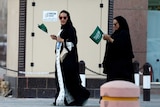 Saudi women hold national flags as they walk on a street