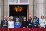 The royal family stands on a balcony.