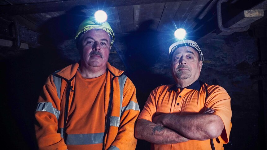 Two men in high vis outfits and miners caps underground