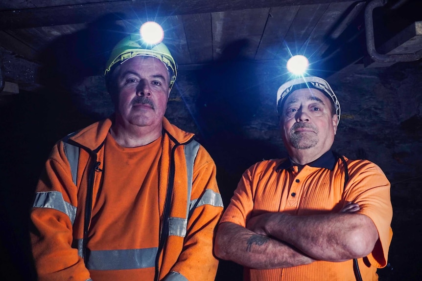 Two men in high vis outfits and miners caps underground