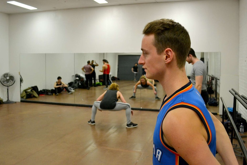 A man stands against a beam in a dance rehearsal studio.
