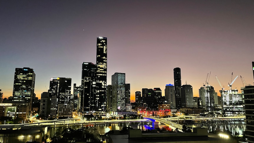 shows first light rising behind tall building with Brisbane River and freeway in the foreground