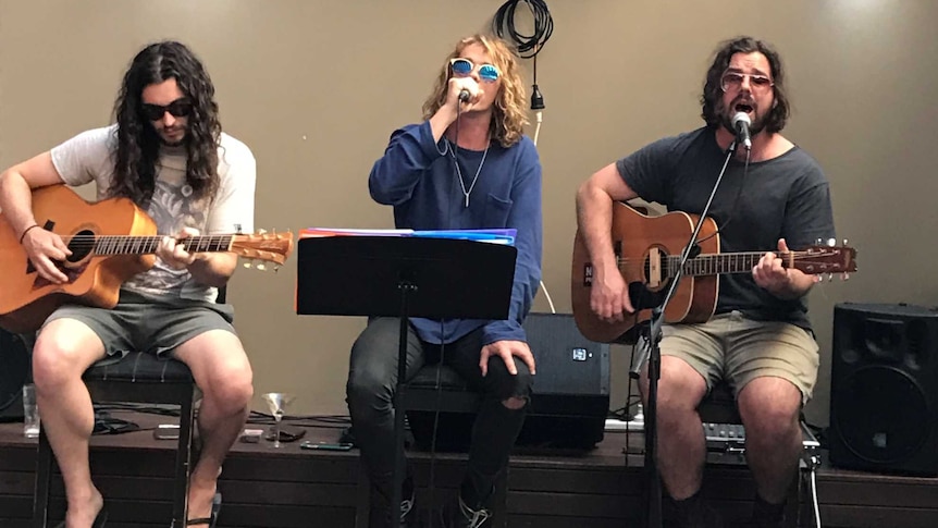 Three people are singing and playing guitar in a courtyard