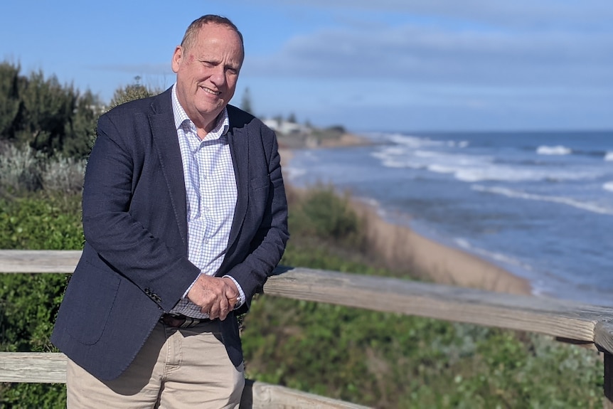 Don Punch leans on a wooden railing, beach in the background. 