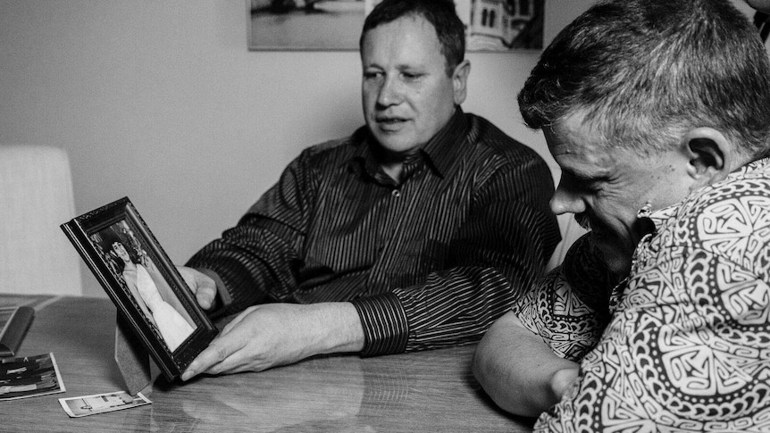 Black and white picture of Mark and Adam James look at a photo of their mother, Maria