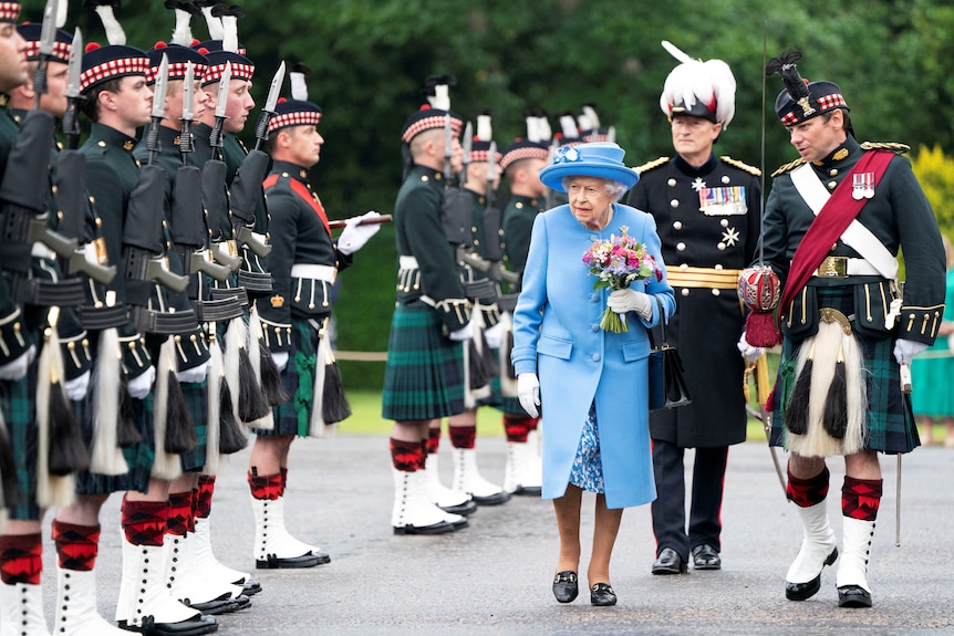 Queen Elizabeth dressed in blue surrounded by people dressed in traditional scottish uniforms with quilts