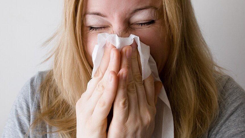 A woman blows her nose on a tissue.