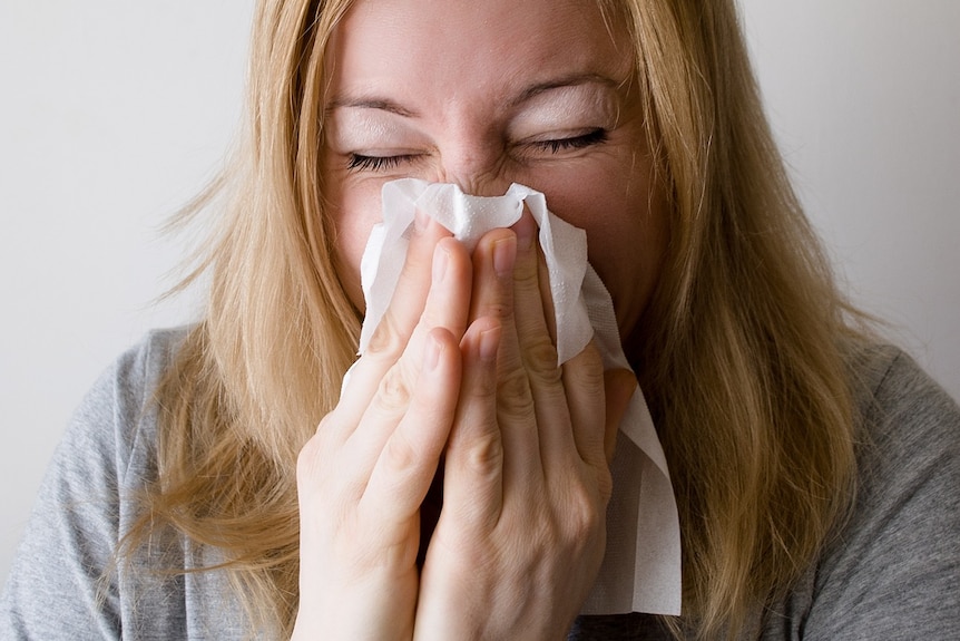 A woman blows her nose on a tissue.