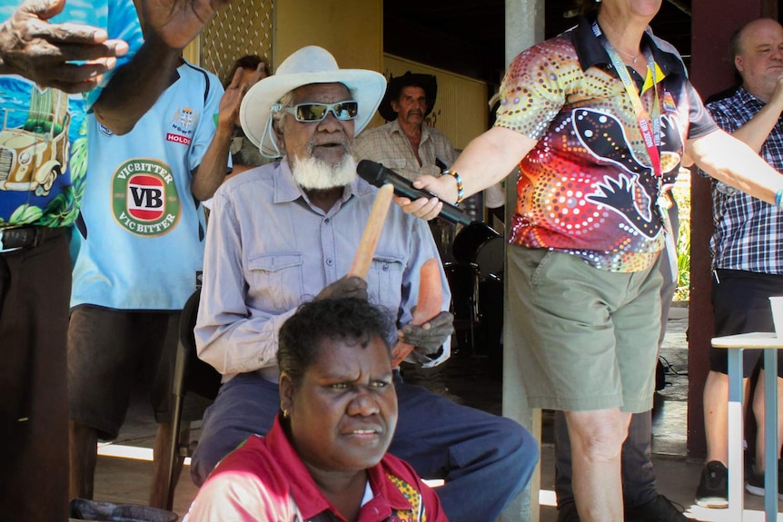 Kowanyama elder Colin Lawrence Snr sings into a microphone with clap sticks during a community day in Kowanyama.