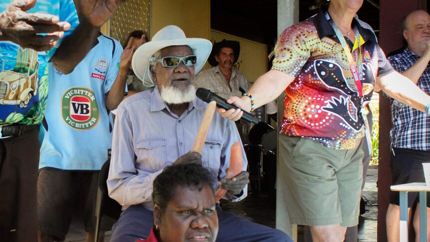 Kowanyama elder Colin Lawrence Snr sings into a microphone with clap sticks during a community day in Kowanyama.