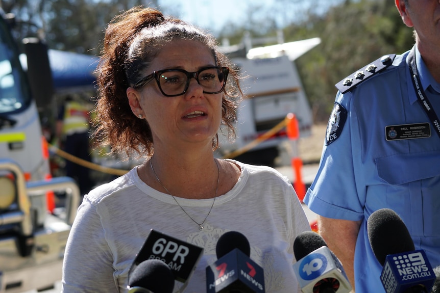 A mid-shot of a middle aged woman with dark hair and spectacles speaking during a media conference outdoors.