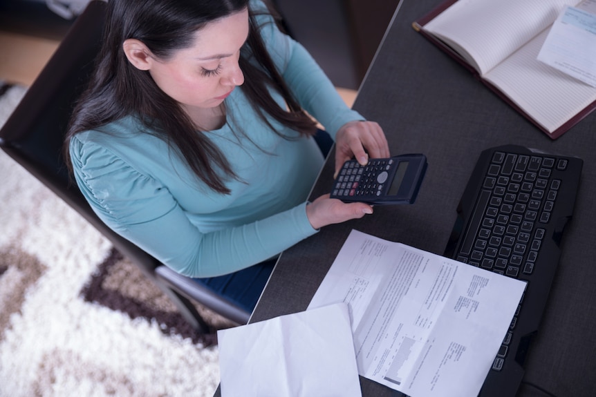 Woman holding calculator surrounded by documents and keyboard on desk.