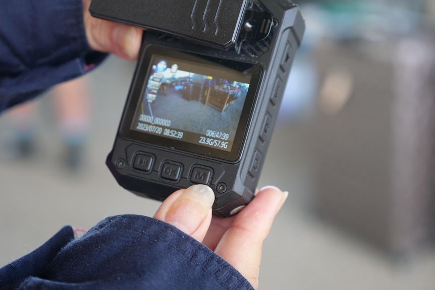 A person holds up a body-worn camera, displaying its screen.