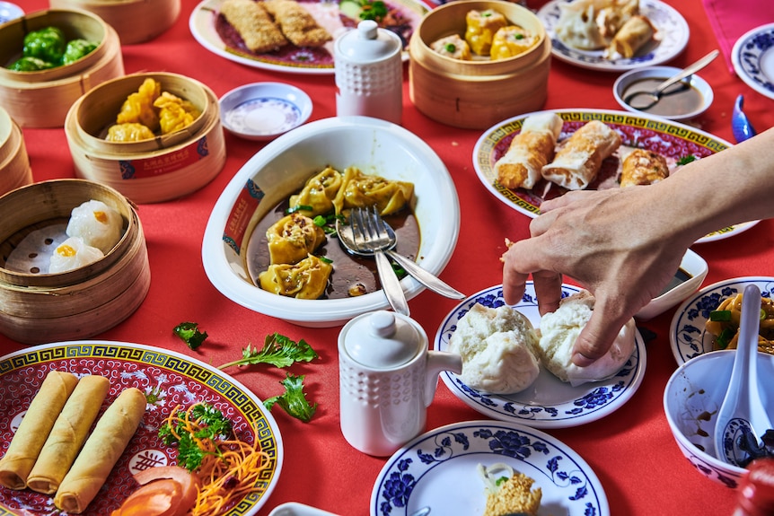 About a dozen different plates of Chinese food on a bright red tablecloth.