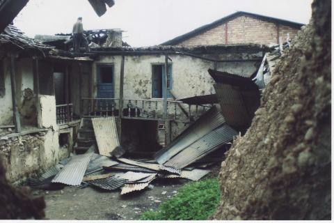 A home stands half damaged with boards and tin laying on the ground.