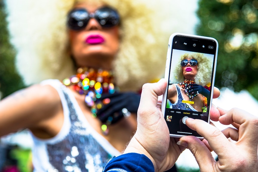 A person in a colourful costume poses for a photograph to be taken on a mobile phone