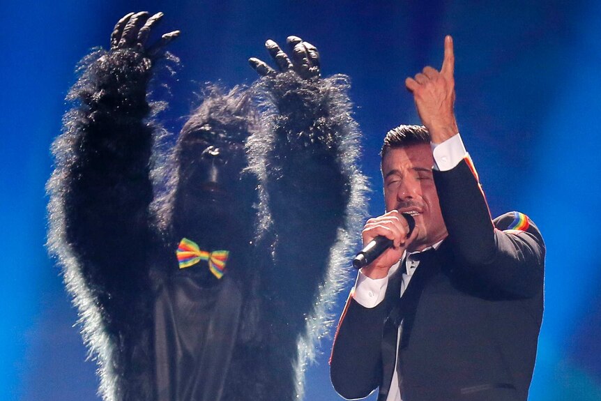 A man in a gorilla suit points to the sky ans Francesco Gabbani sings and raises his right arm to the sky