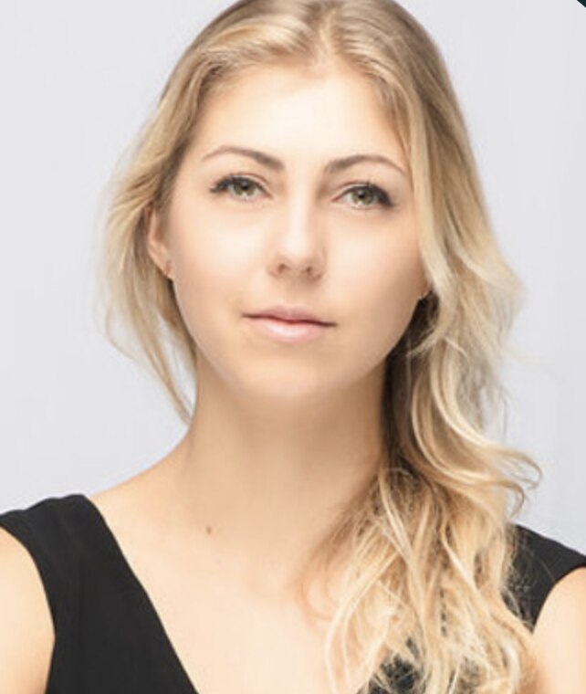 Closely-cropped photo of woman with blonde hair and black sleeveless shift smiles slightly.