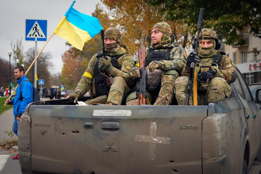 Three armed Ukrainian soldiers sit in the tray of a ute.