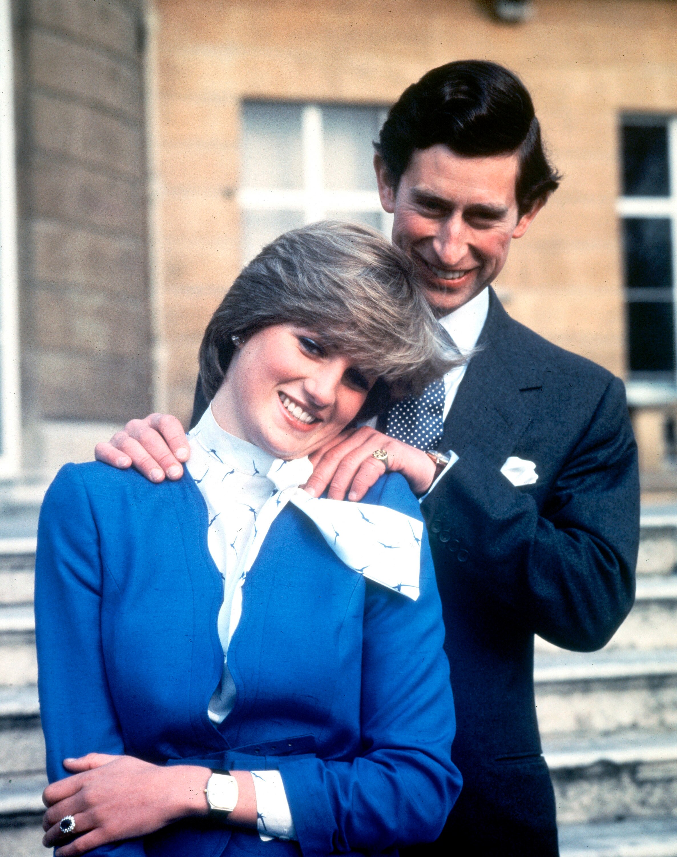 La joven princesa Diana viste un traje azul cobalto con una bufanda blanca y azul, mientras que el príncipe Carlos viste un traje.