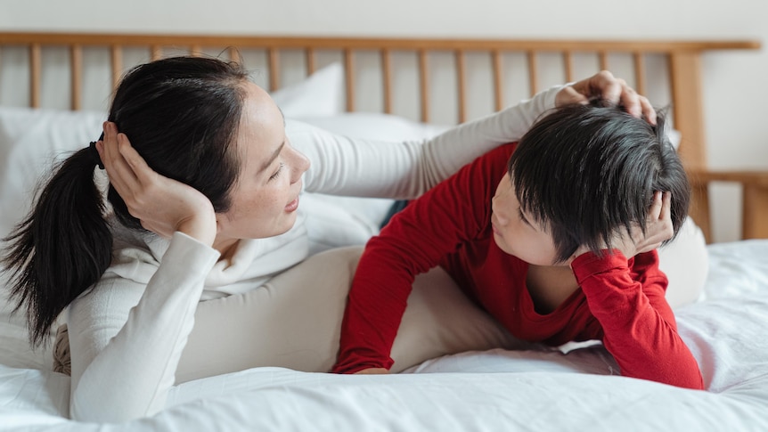 A woman and child lie facing each other on a bed for a story on sharing a child's autism diagnosis