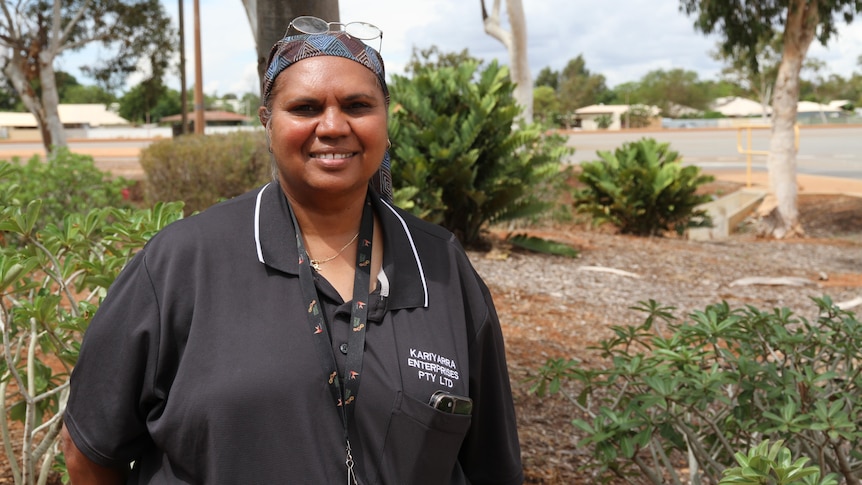 An Indigenous woman smiles at the camera with shrubs behind her 