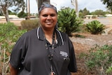 An Indigenous woman smiles at the camera with shrubs behind her 