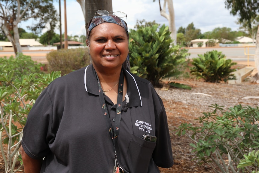 A smiling Indigenous woman standing in front of some shrubs.