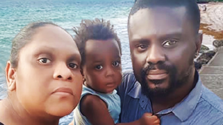 Family of four including a baby, on the beach at Barbados, looking serious.