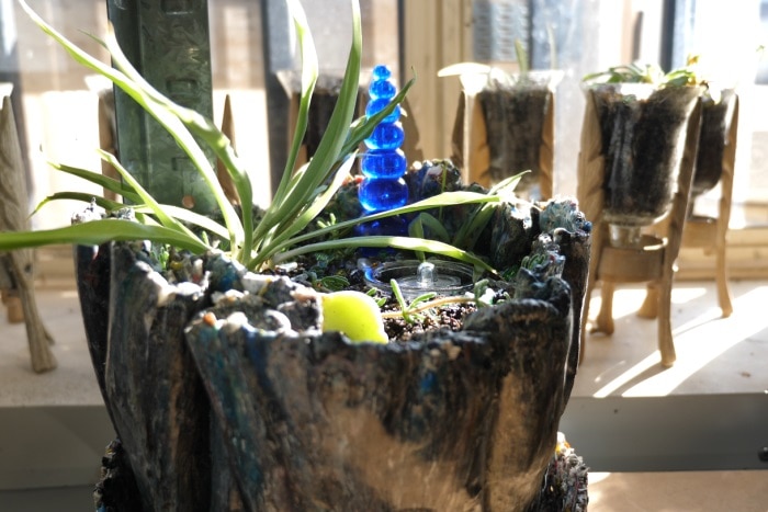 A recycled plastic plant pot, with a succulent in it sitting on a sunny shelf by a window.