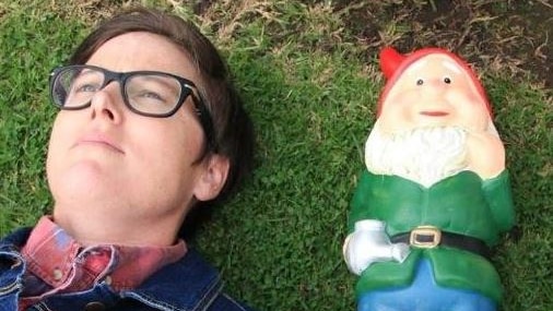 Hannah Gadsby on the grass next to a gnome