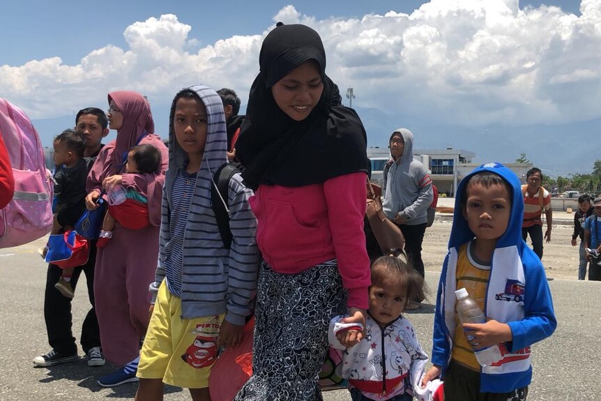 A mother stands on the tarmac of an airport waiting with her three children