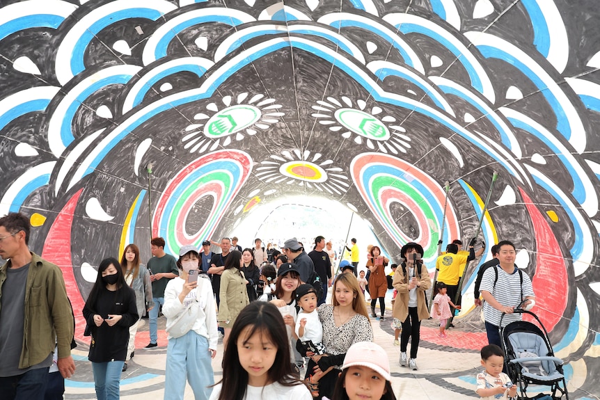 Children smile as they walk through a colourfully painted tunnel in a tourist crowd