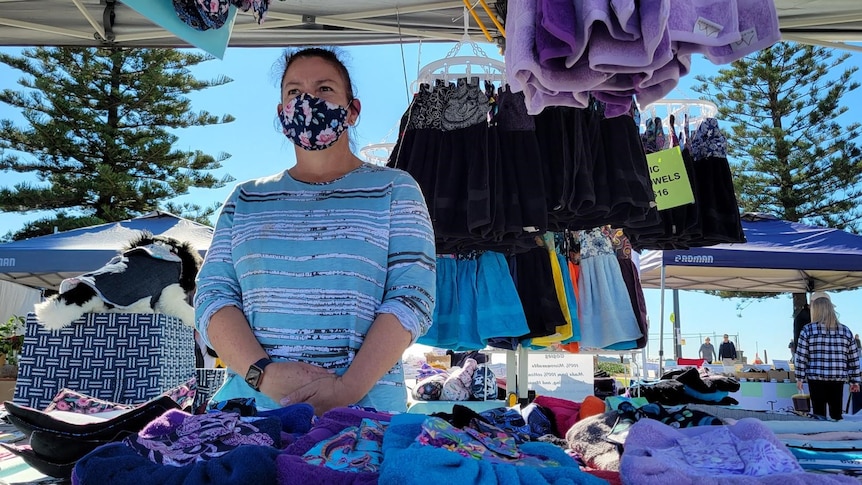 A woman wearing a mask standing behind a table with rows of face masks on top