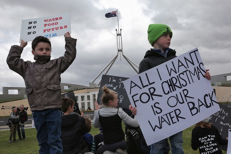 two children hold signs, one reading all i want for christmas is our water back