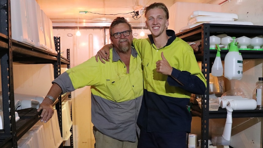 Two men facing the camera in a shipping container filled with crickets