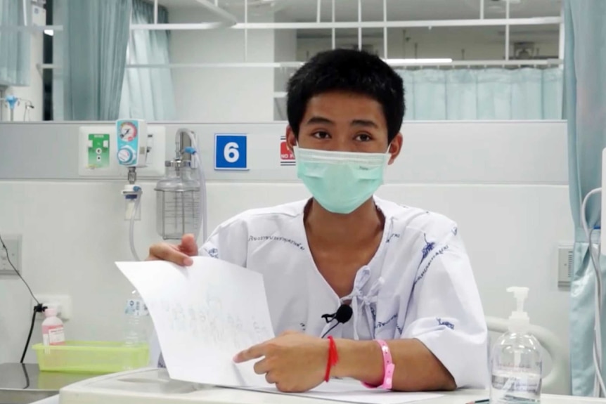 Boy with hospital gown and face masks holds up a drawing