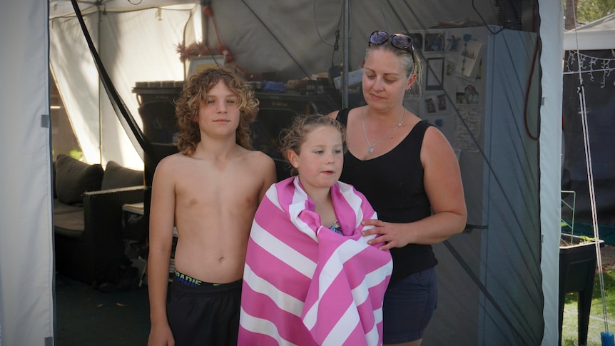A woman and two children stand posing for a photo in front of a gazebo in a caravan park.